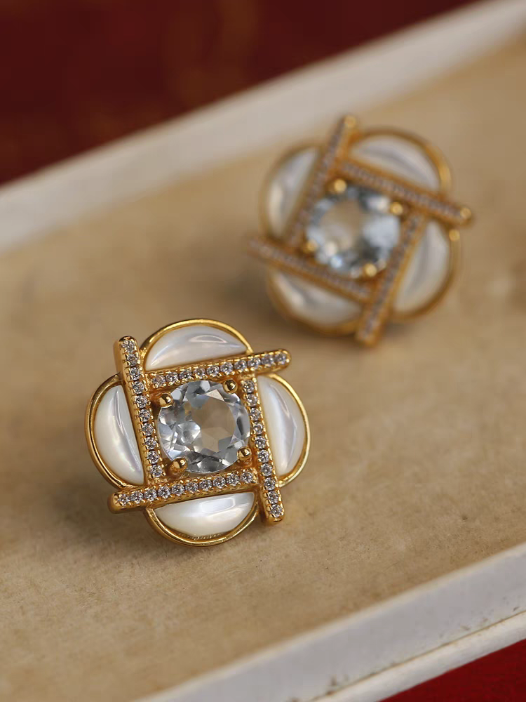 Pendientes de trébol de molino de viento con diseño original de Kemstone, hechos a mano. Pendientes de nácar en plata bañada en oro con detalles de topacio azul cielo.